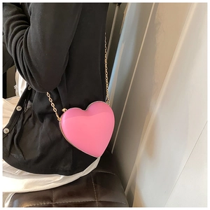 Detail of pink heart-shaped crossbody bag with gold metal trim and chain on black outfit
