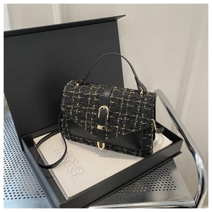 Détail d'un sac à main en tweed noir avec boucle dorée posé sur une boîte de luxe
