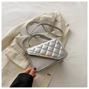 Detail of silver quilted crossbody bag with golden hardware on beige blazer