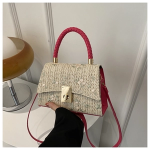 Detail of straw woven handbag featuring floral embroidery and pink woven top handle