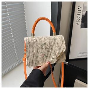 Detail of floral embroidery and orange handle on woven cream crossbody bag for summer