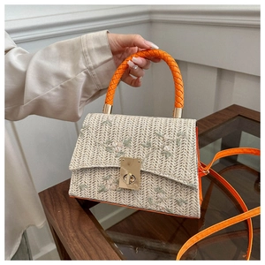 Detail of straw woven tote with floral embroidery and orange tube handles on a desk