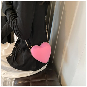 Model wearing a bright pink heart-shaped crossbody bag with a sleek gold chain strap