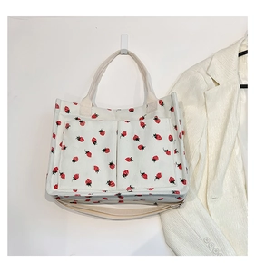 Detail view of corduroy tote bag featuring red strawberry patterns and large front pockets