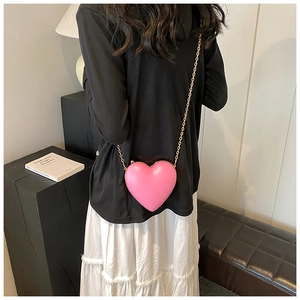 Chic pink heart-shaped crossbody bag with gold chain strap worn by a female model