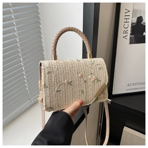 Detailed embroidery of pink flowers and green vines on a beige straw crossbody handbag