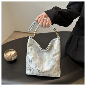 Detail of butterfly embroidery on white bucket bag with blue leather strap and metal hook