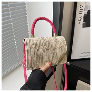 Detail of woven straw bag with floral embroidery and pink circular top handles