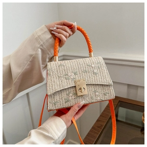 Detail of woven straw handbag featuring floral embroidery and vibrant orange handles