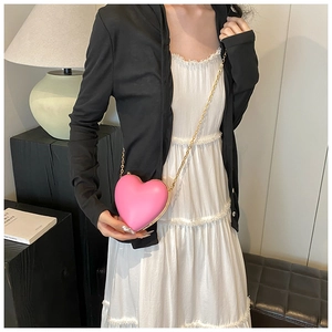 Pink heart-shaped crossbody bag with gold chain strap worn over a white dress