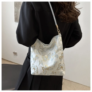 Detail of elegant butterfly embroidery on creamy white shoulder bag with gold hooks