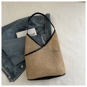 Detailed view of woven straw bucket bag with black leather trim and crossbody strap