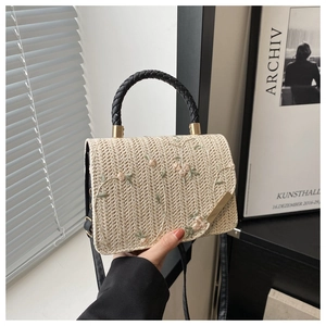 Detail of beige straw bag featuring floral embroidery and black woven handle