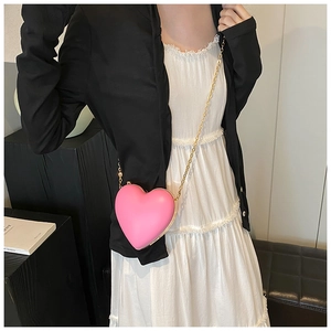 Close-up of pink heart-shaped crossbody bag with gold chain strap on a black stand