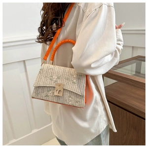 Close-up of woven straw handbag with floral embroidery and vibrant orange handle