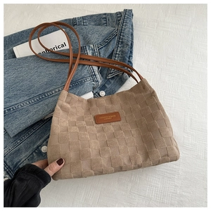 Close-up of brown woven texture shoulder bag with leather logo patch and slim straps