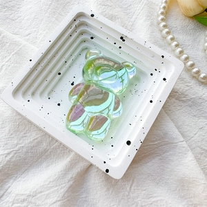 Close-up of a holographic green bear phone grip on a white decorative display tray