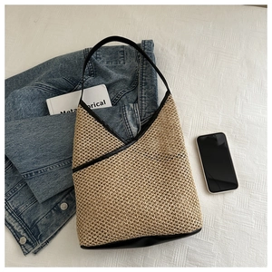 Close-up of handmade straw bucket bag with black leather trim on a white textile background