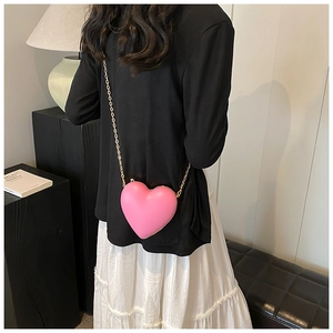 Pink heart-shaped crossbody bag with gold chain strap shown on a model