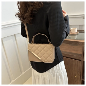 Detail of beige quilted shoulder bag with gold metal trim worn by a model in a cozy room