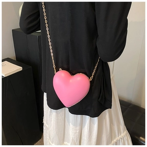 Detail of pink 3D heart-shaped mini bag with gold chain strap worn by model