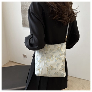 Detailed butterfly embroidery and silver metal hardware on a cream crossbody bucket bag