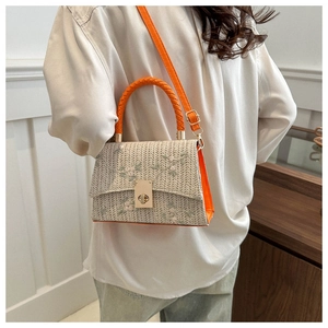 Detail of woven straw bag with floral embroidery, orange leather trim, and metal clasp