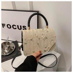 Close-up of woven beige handbag with pink floral embroidery and black ring handle