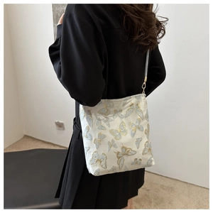 Close-up of golden butterfly embroidery on ivory bucket bag with bamboo leaf patterns