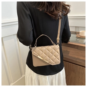 Model wearing a beige quilted crossbody bag with gold hardware in a cafe setting