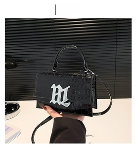 Detail of black crocodile texture bag with gloss finish and M-shaped metal buckle