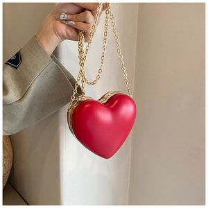 Detail of red heart-shaped clutch bag with gold chain strap held against a grey suit