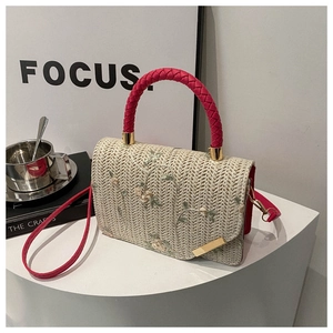 Close-up of floral embroidery on beige straw handbag with fuchsia woven handle and gold hardware