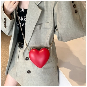 Detail of red heart-shaped crossbody bag with gold chain strap worn by a model