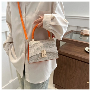 Close-up of woven straw bag with floral embroidery and vibrant orange handles