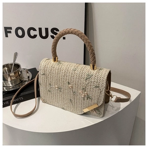 Detail of cream straw handbag with delicate floral embroidery and brown woven handle