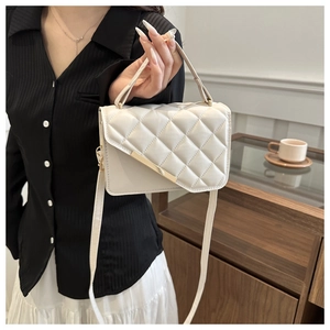 Close-up of quilted cream beige handbag with elegant gold metal bar and top handle