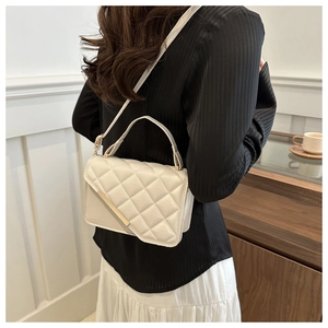 Model wearing a cream quilted crossbody bag with gold metal trim and top handle