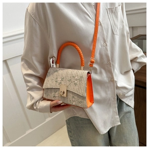 Detail of straw crossbody bag with floral embroidery and orange leather accents on model