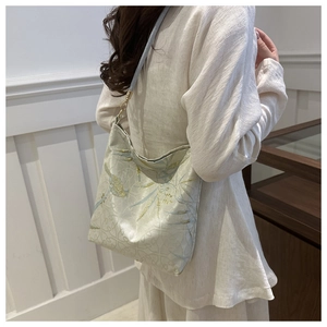 Detailed embroidery of flowers and birds on a silk texture shoulder bag with soft blue strap