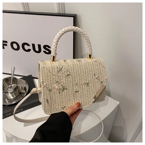 Detail of straw woven crossbody bag featuring floral embroidery and white woven handles