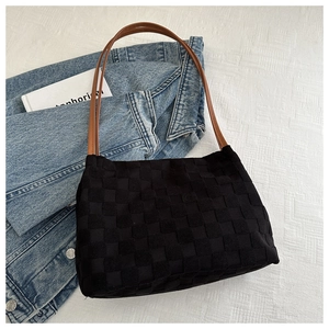 Close-up of black woven checkered texture shoulder bag with slim brown leather straps