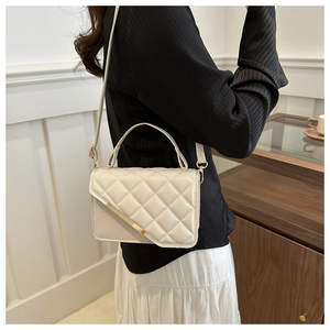 Detail of white quilted crossbody bag with gold metal trim and textured diamond pattern