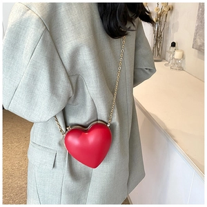 Model wearing a red heart-shaped hard shell crossbody bag with a gold chain strap