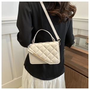 Rear view of a white quilted crossbody bag with gold metal trim worn by a model in a home setting
