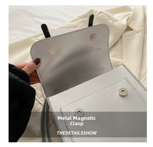 Detail shot of the dual silver magnetic snap buttons on a white square handbag