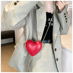 Detail of red heart-shaped shoulder bag with gold chain strap on a grey suit model