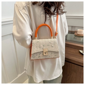 Detail of floral embroidery on a straw woven crossbody bag with orange leather handles