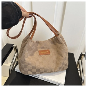 Detail of checkered tote bag with brown leather handles and brand logo patch