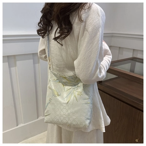 Detail of embroidered magpie and bamboo pattern on a cream-colored oriental shoulder bag